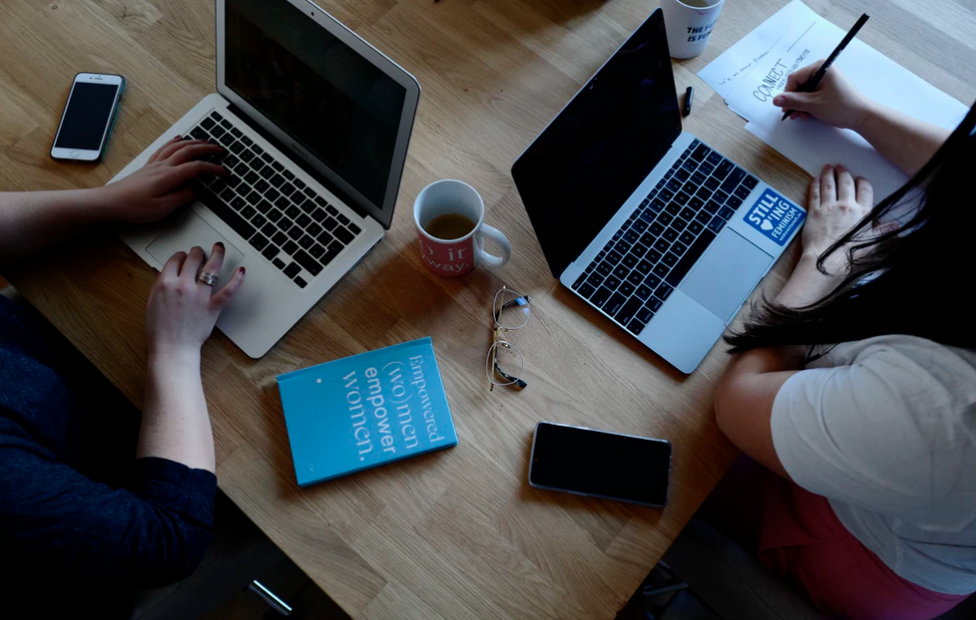 two people sitting at table with laptops, empower women book
