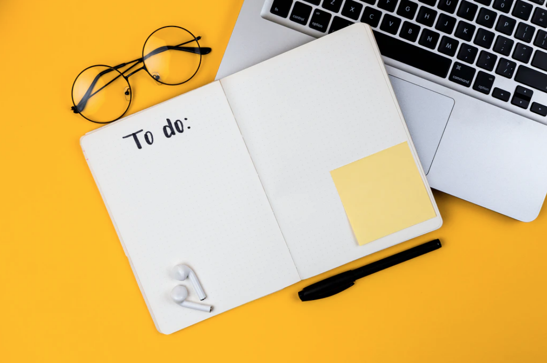 yellow background, glasses, open notebook that says "to do" on open laptop, international students list